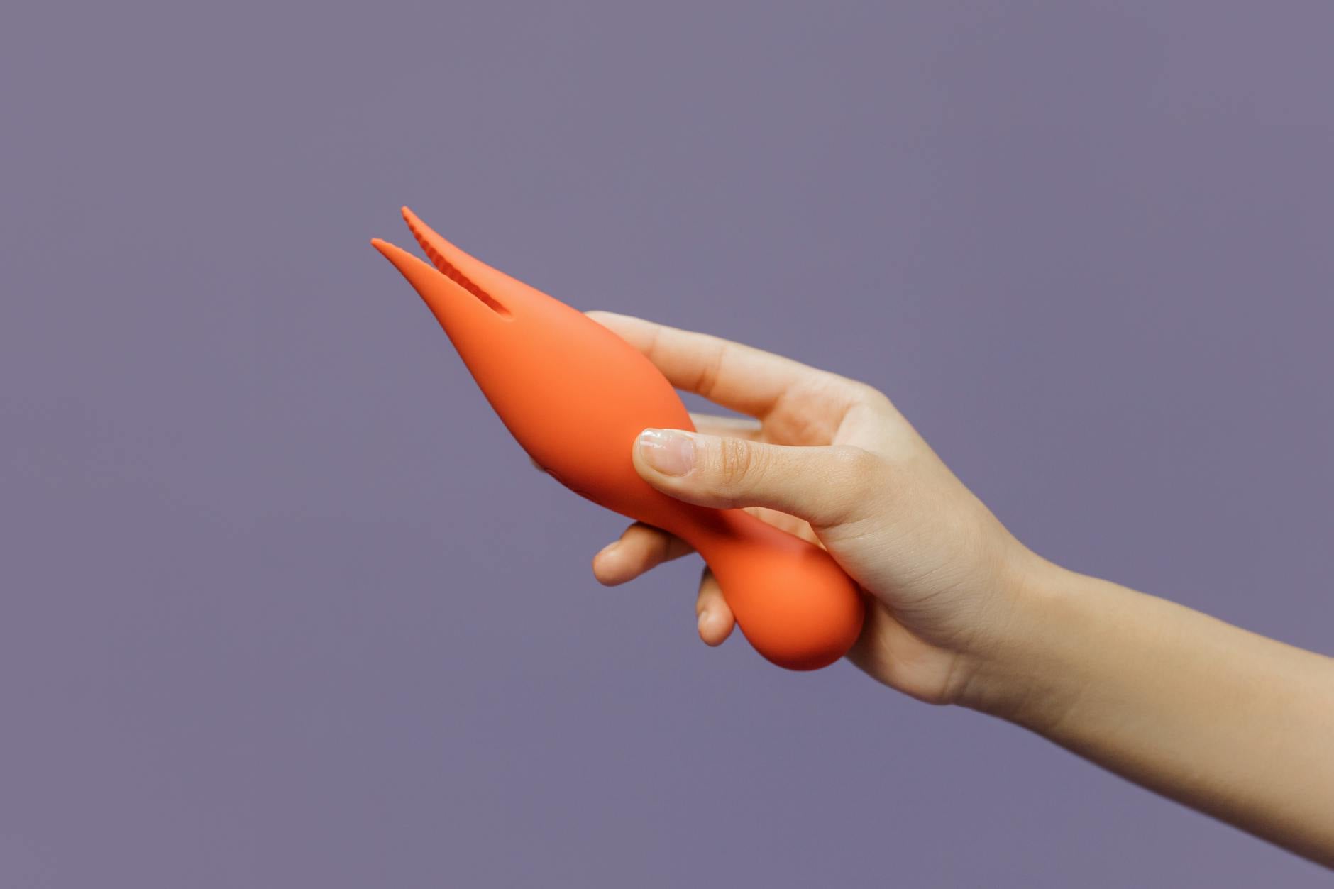 A hand holding a lemon clitoral vibrator against a minimalistic purple backdrop, showcasing modern intimacy.