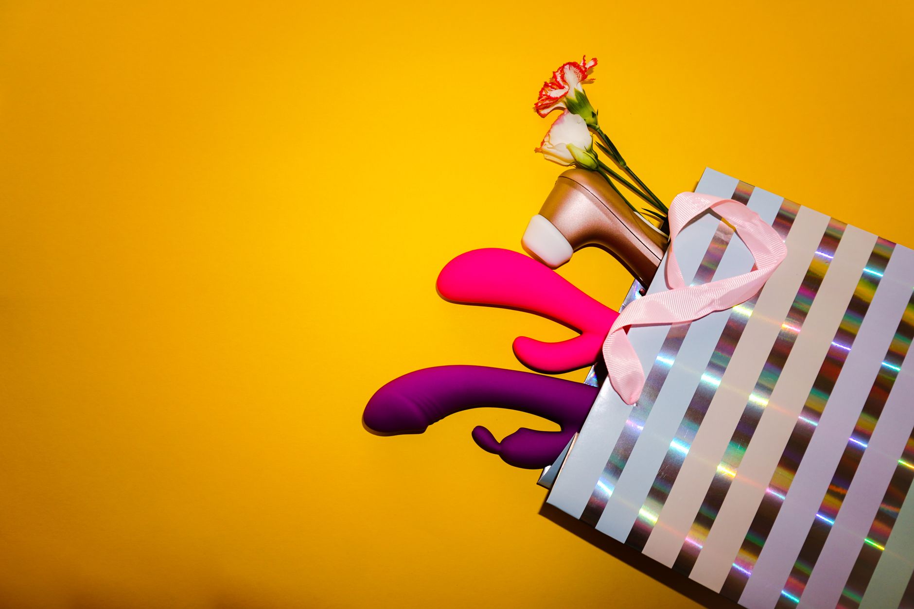 Colorful vibrators with flowers in a holistic gift bag against a bold yellow background