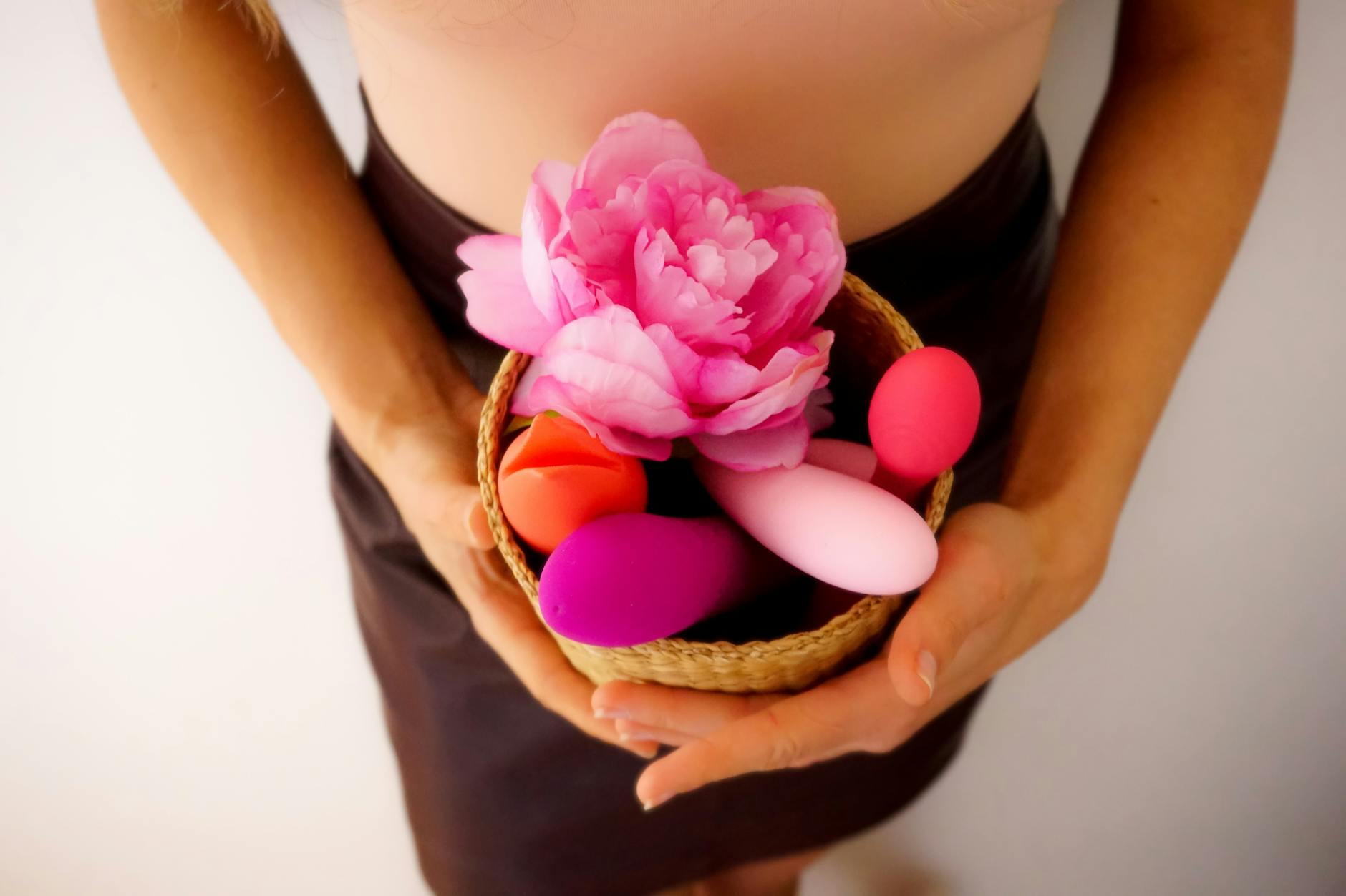 A hand arranging colorful vibrators and wellness items in a basket, representing pleasure recovery and self-care